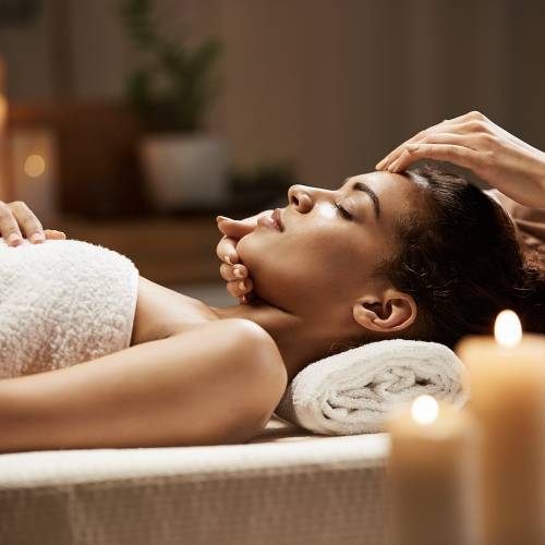 Attractive african girl enjoying face massage in spa salon. Closed eyes.