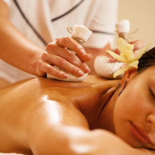 Close-up of relaxed woman getting back massage with herbal balls at health spa.